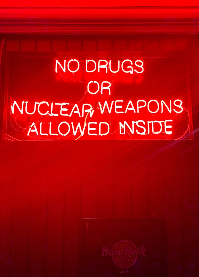 Bright neon sign reading 'No drugs or nuclear weapons allowed inside' in a bar setting.